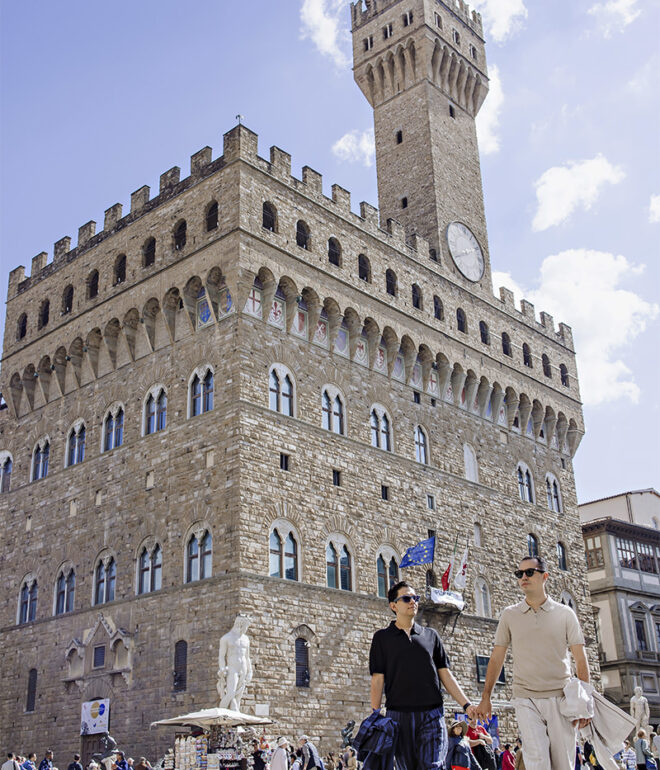 Lalo and Xavi walking hand in hand in front of Palazzo Vecchio during their pre-wedding photoshoot in Florence, Italy — a romantic and cinematic moment captured by Cossu Photography.