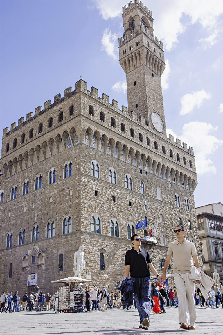 Lalo and Xavi walking hand in hand in front of Palazzo Vecchio during their pre-wedding photoshoot in Florence, Italy — a romantic and cinematic moment captured by Cossu Photography.