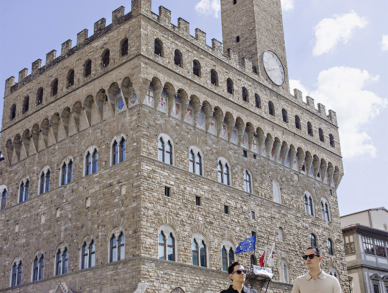Lalo and Xavi walking hand in hand in front of Palazzo Vecchio during their pre-wedding photoshoot in Florence, Italy — a romantic and cinematic moment captured by Cossu Photography.