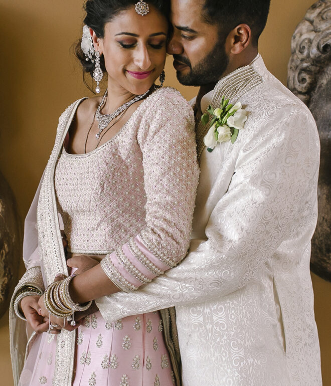 Couple at a Tuscany wedding posing in an intimate portrait; the groom embraces the bride wearing a pink embroidered lehenga and traditional jewelry.