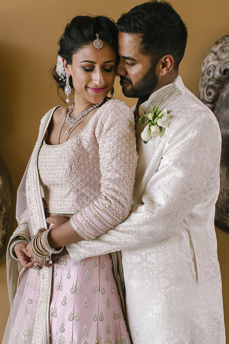 Couple at a Tuscany wedding posing in an intimate portrait; the groom embraces the bride wearing a pink embroidered lehenga and traditional jewelry.