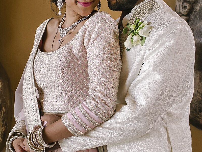 Couple at a Tuscany wedding posing in an intimate portrait; the groom embraces the bride wearing a pink embroidered lehenga and traditional jewelry.