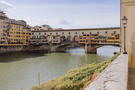 Romantic moment of Lalo and Xavi at Ponte Vecchio in Florence, framed by the Arno River and golden sunset — timeless pre-wedding photography by Cossu Photography.