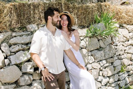 Dan and Sophie smiling beside a rustic stone wall in Tuscany